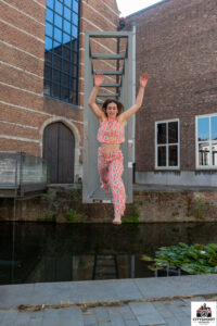 Jonge vrouw springt enthousiast door de lucht voor een stalen constructie aan de Melaan bij de Minderbroederskerk tijdens een dynamische Cityshoot in Mechelen door fotograaf Stef Boey